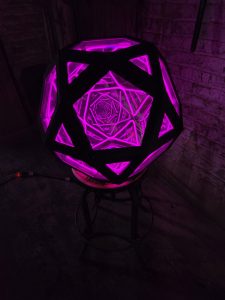Vibrant purple geometric LED art sculpture by Chris Knight Creations in a rustic room setting.