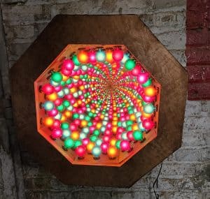 Colorful illuminated LED art sculpture on wooden wall, vibrant modern decor piece.