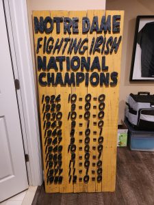 Vintage Notre Dame Fighting Irish Champions wooden sign with years and scores.