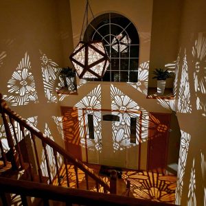 Intricate shadow patterns created by a decorative pendant light illuminating a hallway.