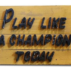 Playful wooden sign with black 3D letters reading "Play Like A Champion Today".