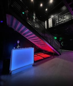 Colorful urban event space with neon lighting and modern staircase indoors.