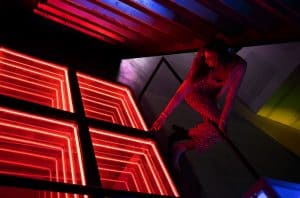 Vibrant red neon geometric art installation with a woman in patterned attire interacting creatively.